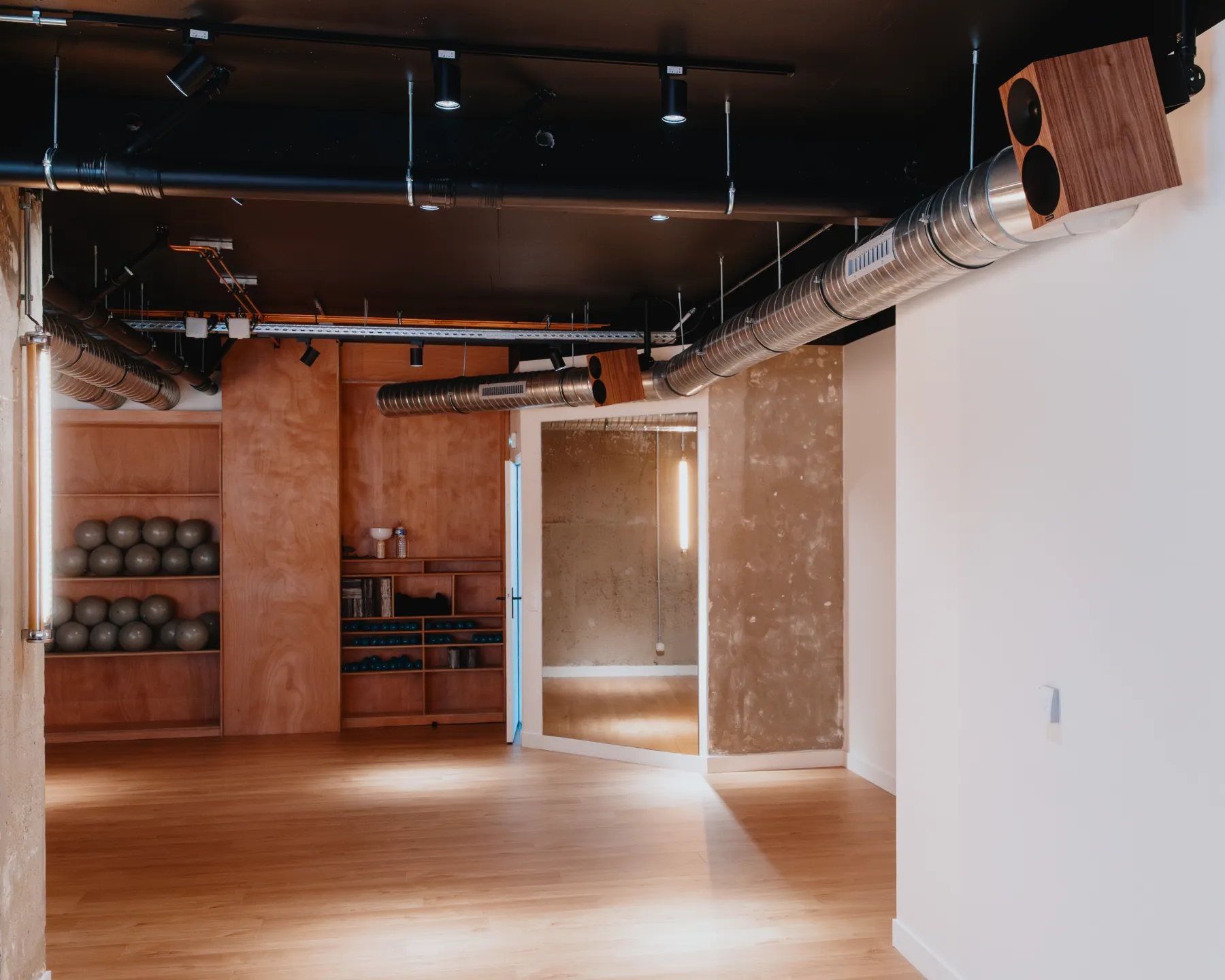 Slowe Wellness House, Paris : studio au parquet clair, enceintes en bois fixées en hauteur sous un plafond noir