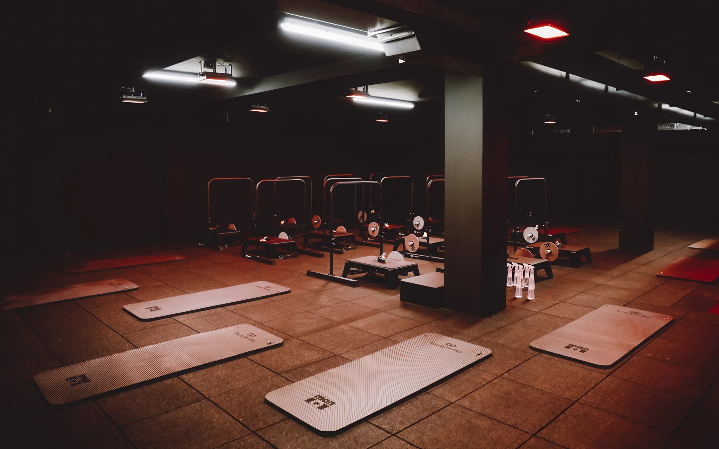 Salle de cours collectif avant la séance : tapis, steps et barres chargées sous un éclairage rouge